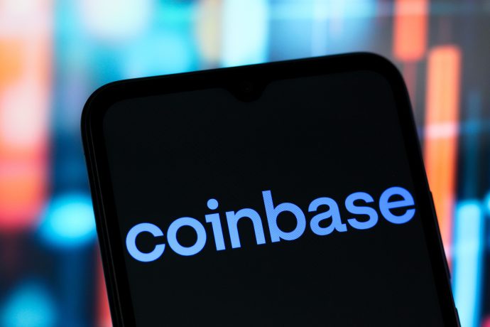 Ein Smartphone zeigt das Coinbase-Logo auf seinem Bildschirm vor einem Hintergrund aus verschwommenen, bunten vertikalen Balken.