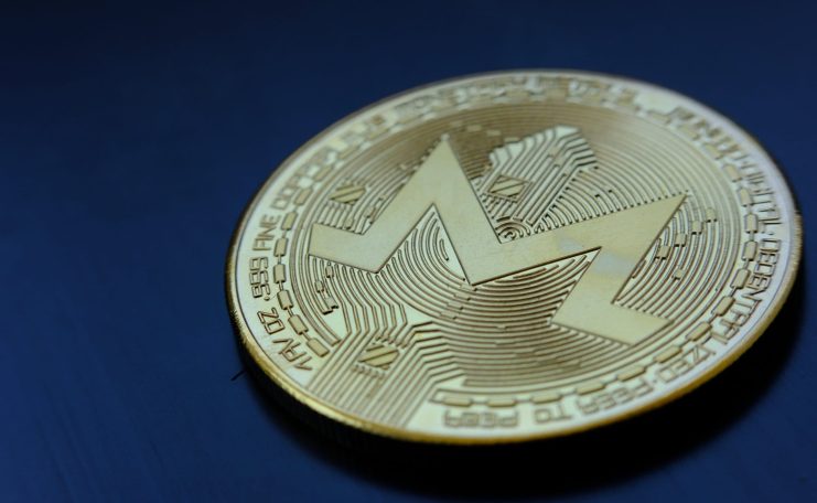 Eine goldene Monero-Kryptowährungsmünze mit dem Monero-Logo liegt auf einer dunkelblauen Oberfläche.