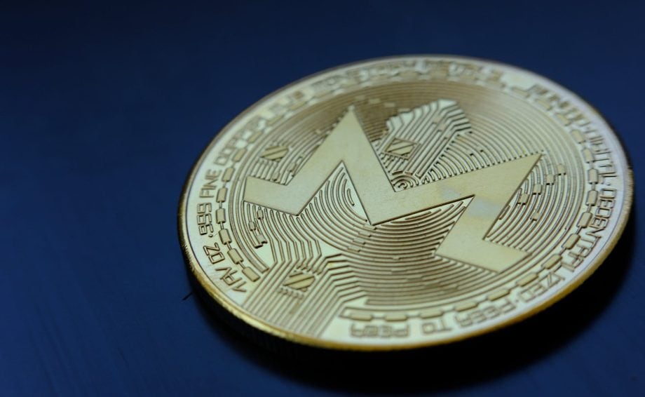Eine goldene Monero-Kryptowährungsmünze mit dem Monero-Logo liegt auf einer dunkelblauen Oberfläche.