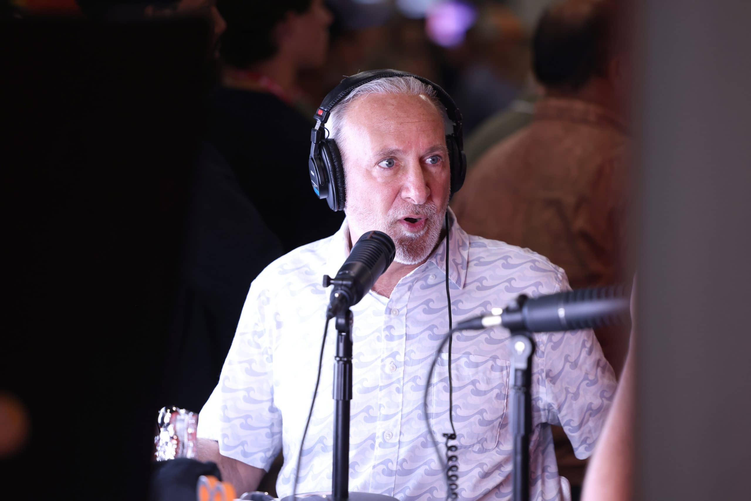 Ein Mann mit Kopfhörern, der Peter Schiff ähnelt, spricht während einer Aufnahme oder eines Interviews in ein Mikrofon und trägt ein gemustertes weißes Hemd.