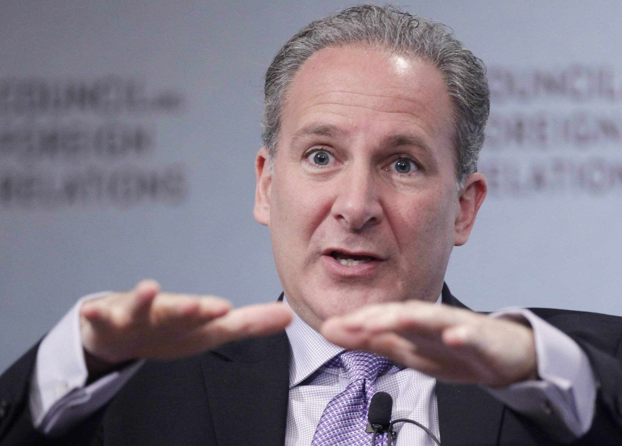 Peter Schiff, im Anzug, gestikuliert mit beiden Händen, während er auf einer öffentlichen Veranstaltung spricht, ein Mikrofon an seiner Krawatte befestigt und ein verschwommener Hintergrund hinter ihm.