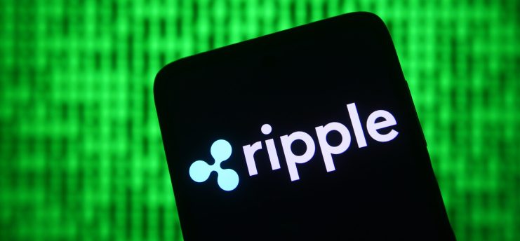 Auf einem Smartphone-Bildschirm werden das Logo und der Name von Ripple vor einem grünen, matrixartigen Binärcode-Hintergrund angezeigt, wodurch Ripples Verbindung zur digitalen Technologie hervorgehoben wird.