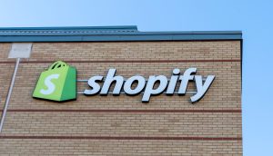Das Logo und der Name von Shopify sind deutlich sichtbar an der äußeren Backsteinmauer eines Gebäudes angebracht und heben sich vom klaren blauen Himmel ab.