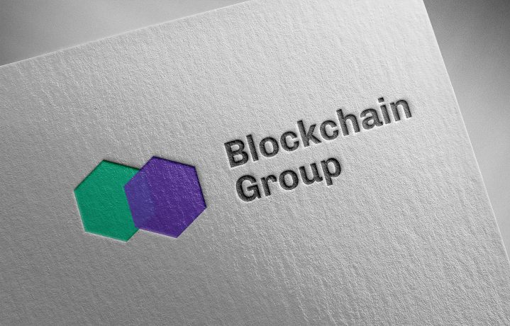 Geprägtes Logo der Blockchain Group mit sich überlappenden grünen und violetten Sechsecken auf strukturiertem weißem Papier, mit einem dezenten, von Bitcoin inspirierten Design.