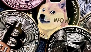 Physische Münzen, die Bitcoin, Ethereum und Dogecoin repräsentieren – angeführt von einem prominenten Dogecoin mit dem Shiba Inu-Hund und dem Wort WOW – fangen das Aussehen eines automatisch gespeicherten Entwurfs digitaler Währungssymbole ein.