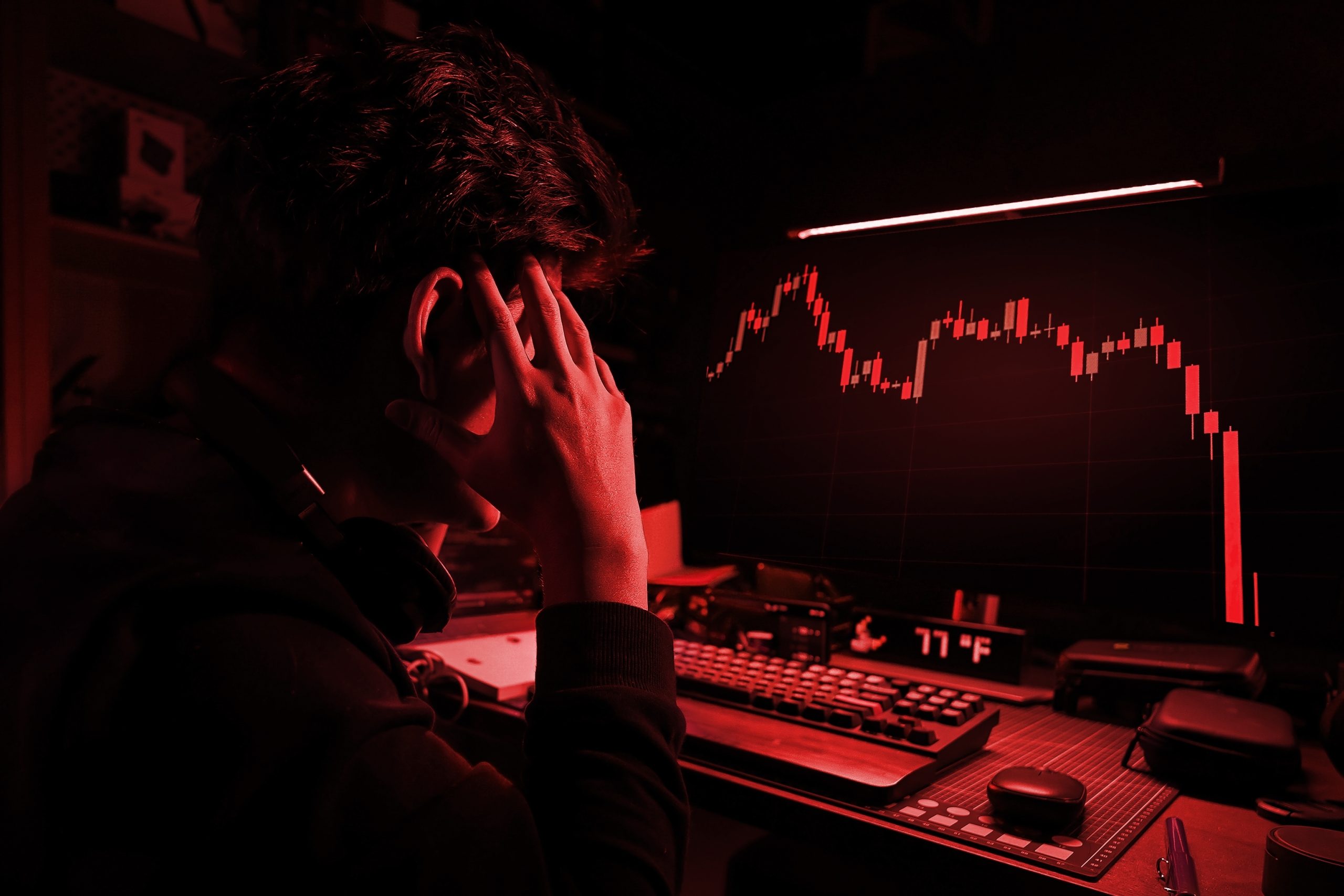 Eine Person sitzt an einem Schreibtisch, blickt auf einen Computerbildschirm in einem schwach beleuchteten Raum und beobachtet den starken Rückgang von Bitcoin auf einem roten Börsenchart.