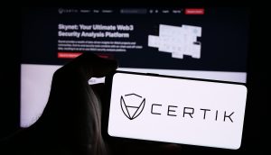 Eine Hand hält ein Smartphone mit dem CertiK-Logo vor einem Computerbildschirm, auf dem die Web3-Sicherheitsanalyseplattform von CertiK präsentiert wird, und betont damit ihre wichtige Rolle beim Schutz von Krypto-Vermögenswerten.