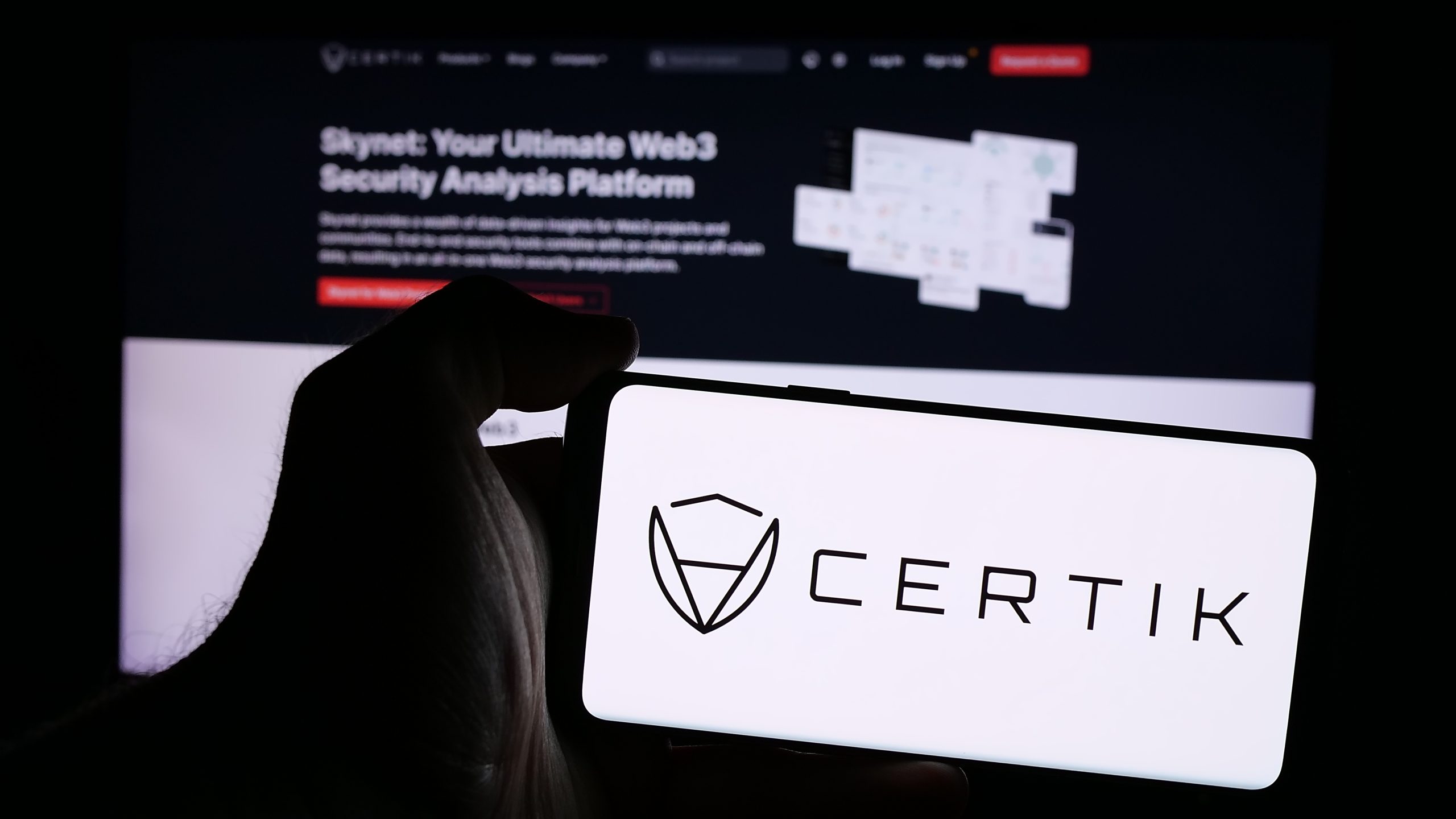Eine Hand hält ein Smartphone mit dem CertiK-Logo vor einem Computerbildschirm, auf dem die Web3-Sicherheitsanalyseplattform von CertiK präsentiert wird, und betont damit ihre wichtige Rolle beim Schutz von Krypto-Vermögenswerten.