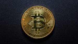 Eine goldfarbene physische Bitcoin-Münze mit dem Bitcoin-Symbol auf einem dunklen strukturierten Hintergrund.