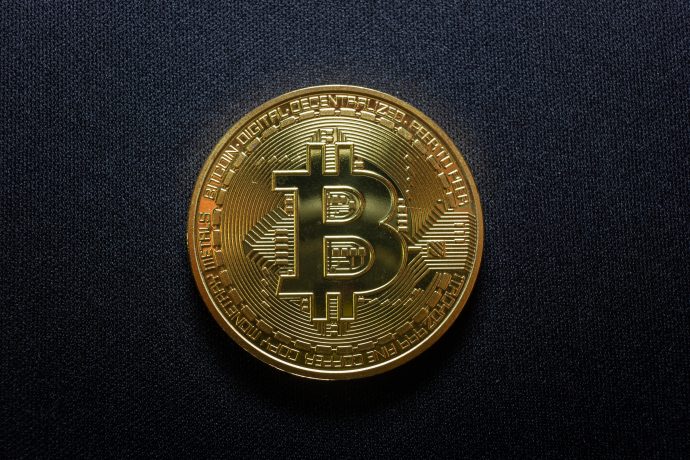 Eine goldfarbene physische Bitcoin-Münze mit dem Bitcoin-Symbol auf einem dunklen strukturierten Hintergrund.