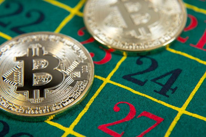 Zwei Bitcoin-Token liegen auf einem grünen Roulettetisch und verdecken teilweise die Zahlen 23, 24 und 27.