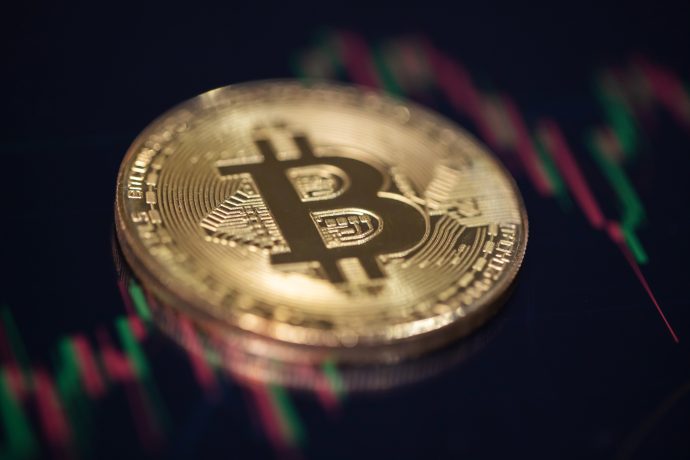 Eine physische Bitcoin-Münze ruht auf einer dunklen Oberfläche, mit verschwommenen Finanzdiagrammlinien im Hintergrund.