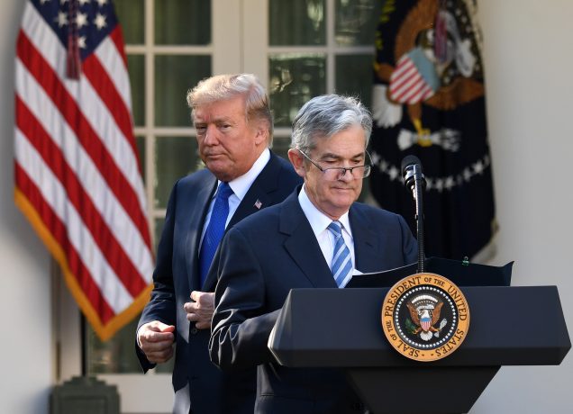 Donald Trump steht hinter Jerome Powell, der an einem Podium mit dem Siegel des Präsidenten spricht; im Hintergrund sind die US-Flagge und die Flagge des Präsidenten zu sehen.