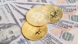 Drei goldfarbene Bitcoin-Münzen liegen auf mehreren ausgebreiteten US-Hundertdollarscheinen.