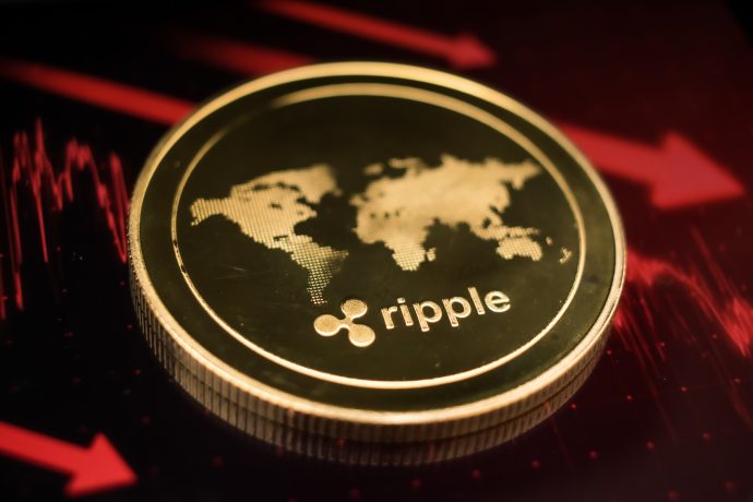 Eine Ripple (XRP)-Münze mit einer Weltkarte steht vor einem Hintergrund aus roten Abwärtspfeilen und Candlestick-Charts, die den jüngsten Kursrückgang von XRP verdeutlichen.