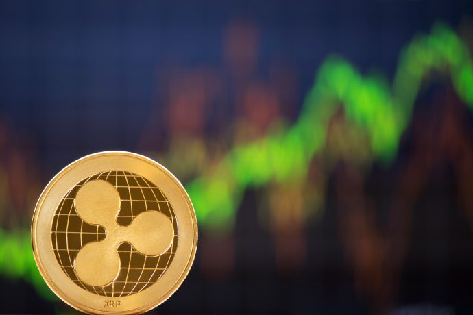 Im Mittelpunkt steht eine goldene XRP-Kryptowährungsmünze mit einem unscharfen grünen und roten Börsendiagramm im Hintergrund.