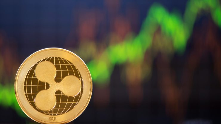 Im Mittelpunkt steht eine goldene XRP-Kryptowährungsmünze mit einem unscharfen grünen und roten Börsendiagramm im Hintergrund.