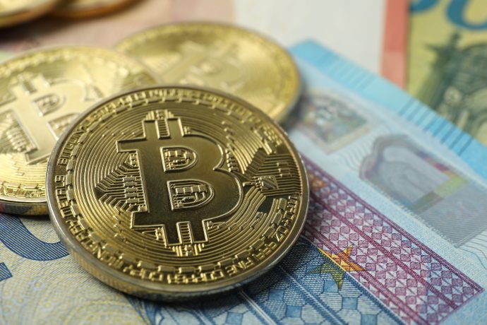Nahaufnahme von physischen Bitcoin-Token, die auf verschiedenen Euro-Banknoten platziert sind und das Konzept von 1.000 Euro in Bitcoin investieren illustrieren.