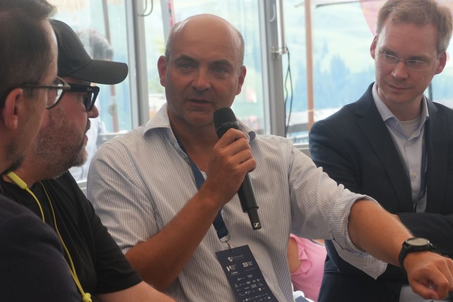 Bernhard 21shares Ein Mann in einem hellen Hemd spricht in ein Mikrofon, während er mit drei anderen Personen bei einer Veranstaltung in einer Halle in Europa über Änderungen und Trends bei Krypto-ETFs diskutiert.