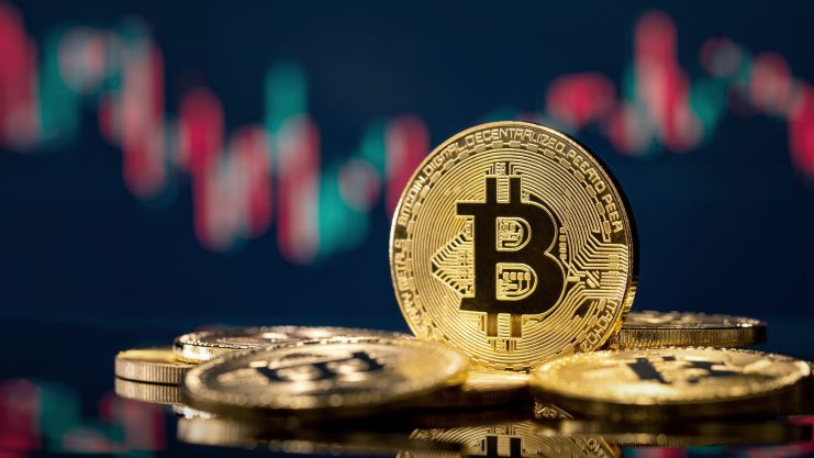 Ein Stapel physischer Bitcoin-Token liegt auf einer spiegelnden Oberfläche, während ein digitales Bitcoin-Finanzdiagramm im Hintergrund verschwimmt.
