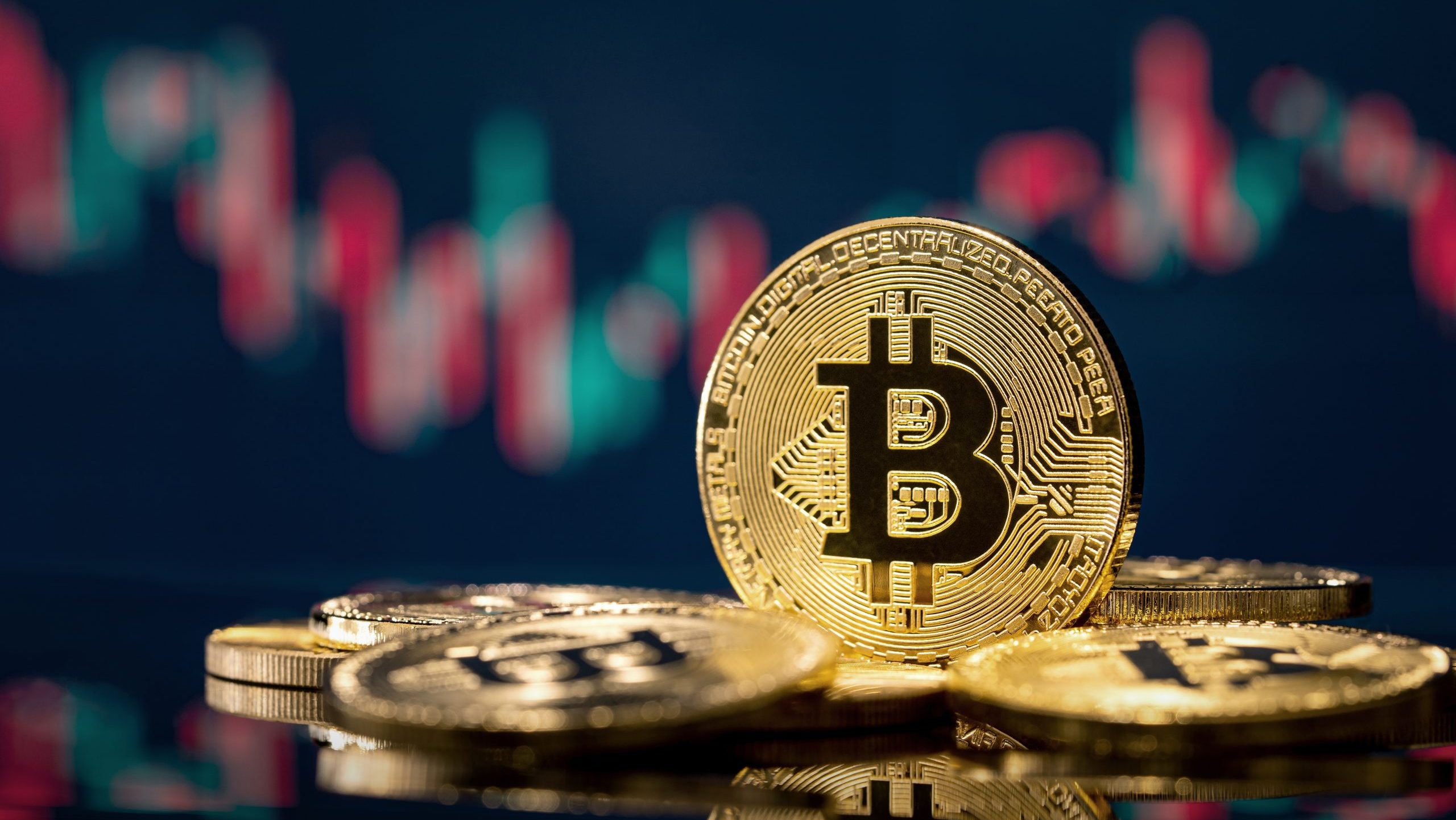 Ein Stapel physischer Bitcoin-Token liegt auf einer spiegelnden Oberfläche, während ein digitales Bitcoin-Finanzdiagramm im Hintergrund verschwimmt.