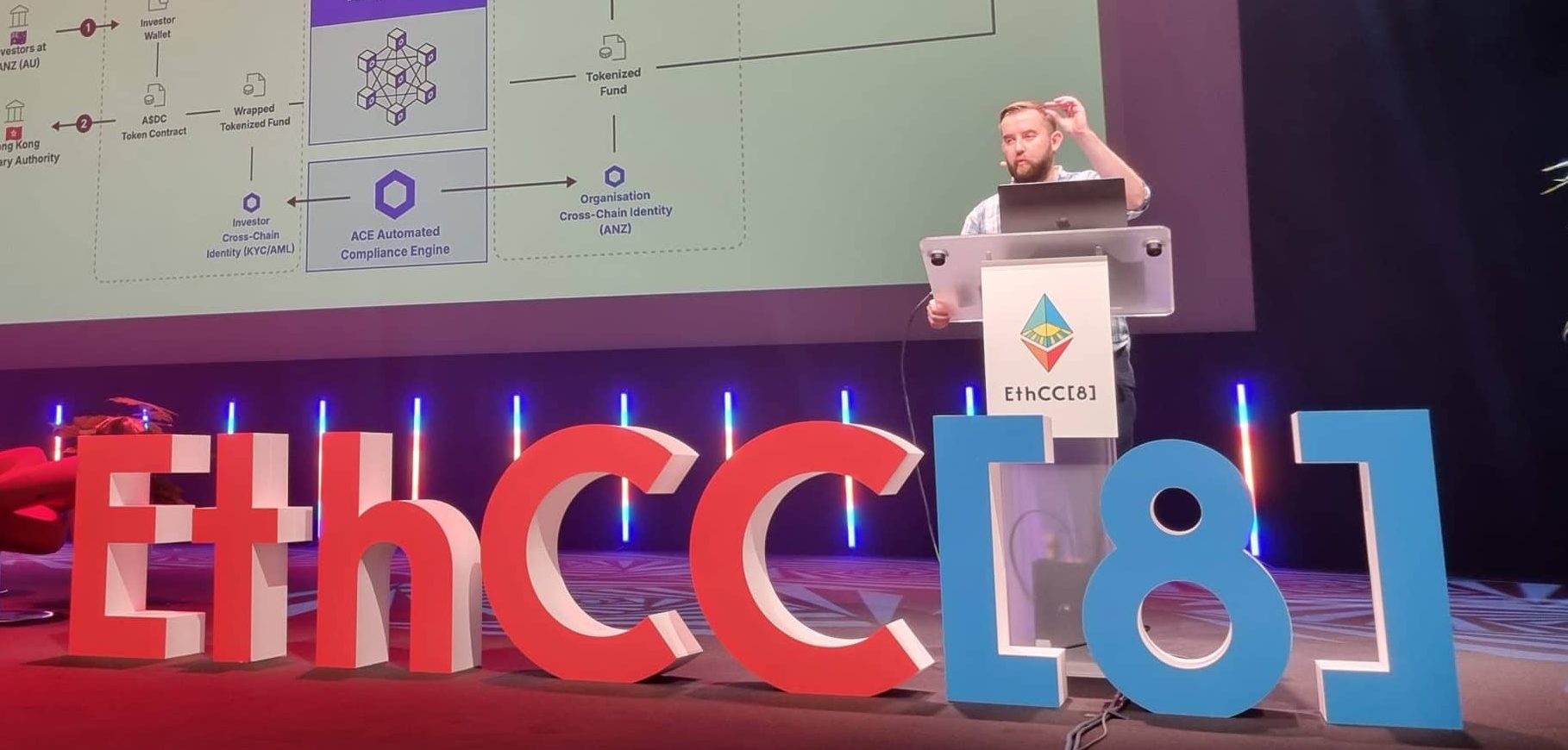 Chainlink-Gründer Sergey Nazarov präsentiert auf der EthCC[8]-Konferenz auf einer Bühne mit großen dekorativen Veranstaltungsbuchstaben und farbenfroher Beleuchtung ein technisches Diagramm zu Fonds-Tokenisierung, Chainlink-Integration und Cross-Chain-Compliance.