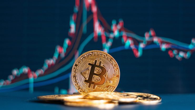 Mehrere goldglänzende Bitcoin-Münzen sind vor einem digitalen Finanzdiagramm mit schwankenden roten und blauen Linien platziert.