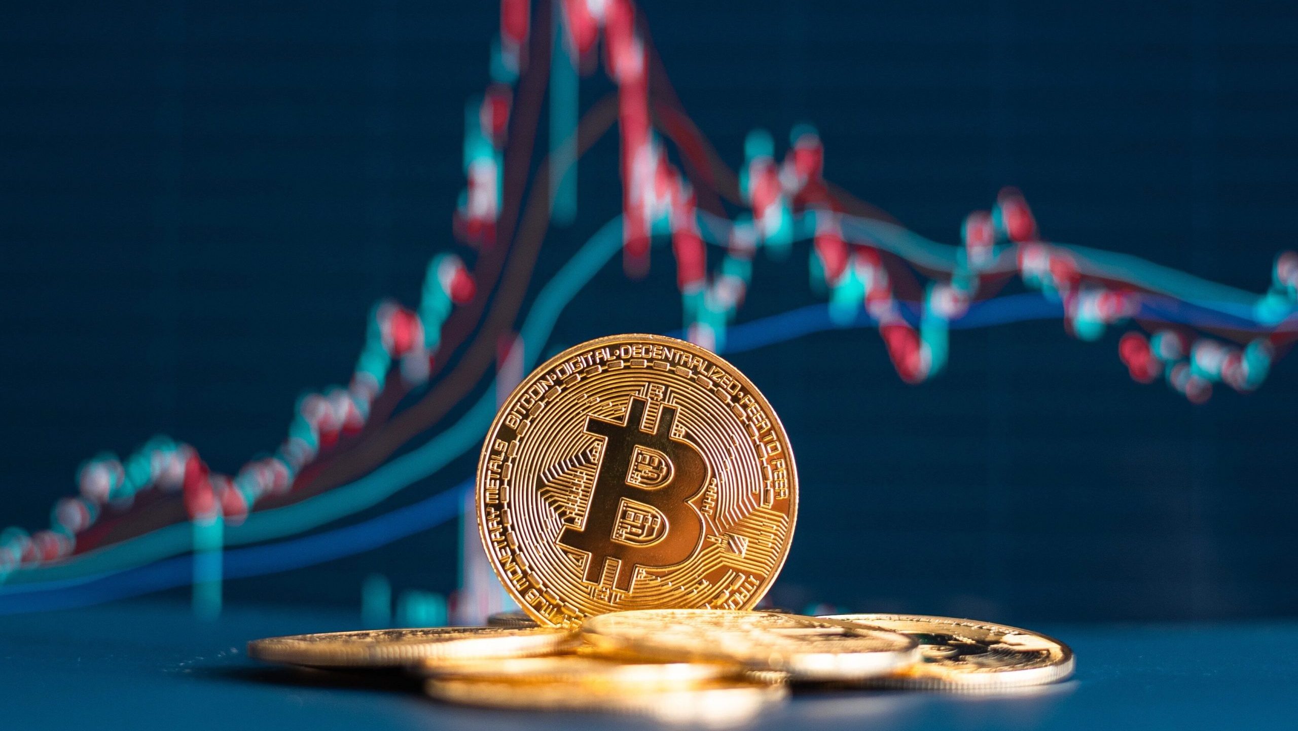 Mehrere goldglänzende Bitcoin-Münzen sind vor einem digitalen Finanzdiagramm mit schwankenden roten und blauen Linien platziert.