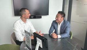 Zwei Männer in Business-Kleidung sitzen sich an einem runden Tisch in einem modernen Büro gegenüber und unterhalten sich über Zugang zu Kapital und Trends in der Krypto-Branche.