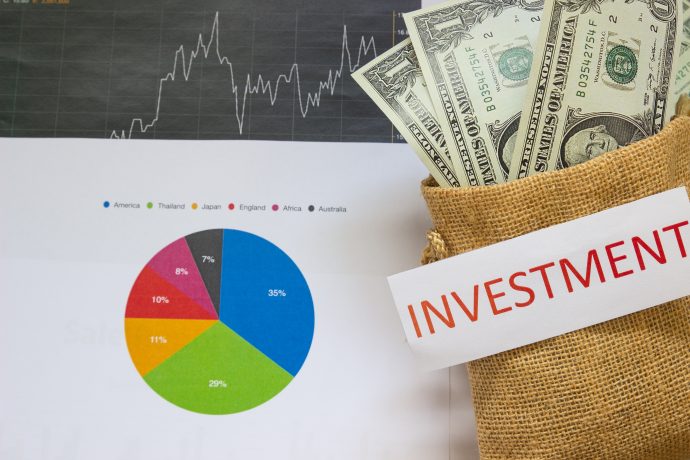 Ein Jutesack mit der Aufschrift "Investment" enthält Dollarscheine, daneben ein Tortendiagramm und ein Börsendiagramm mit Finanzdaten, die Trends in DeFi aufzeigen.