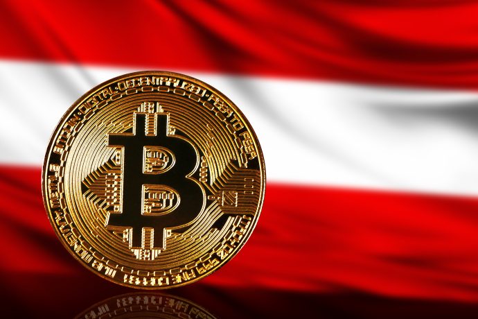 Eine goldene Bitcoin-Münze, die Krypto symbolisiert, ist vor der österreichischen Flagge mit ihren charakteristischen rot-weiß-roten Querstreifen zu sehen.