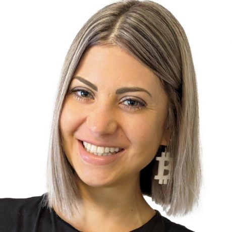 Eine Frau mit glattem, schulterlangem hellbraunem Haar lächelt in die Kamera. Sie trägt große, weiße Ohrringe in Form des Bitcoin-Symbols und feiert damit ihre Nominierung für den 2025 Influencer Award.