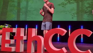 Vitalik Buterin spricht auf der Bühne des EthCC, während im Hintergrund große rote EthCC-Buchstaben und eine Präsentationsfolie über statische HTML-Seiten, Ethereum und IPFS projiziert werden.