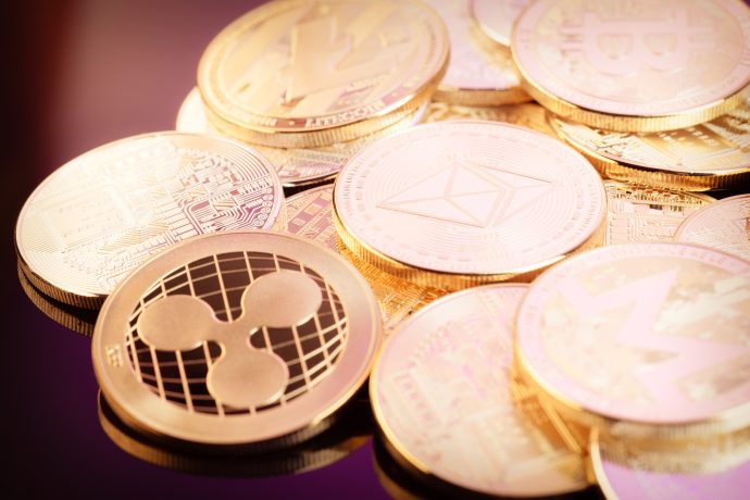 Verschiedene physische Münzen mit den Logos von Kryptowährungen wie XRP, Ethereum, Bitcoin und Litecoin sind gestapelt und verstreut.