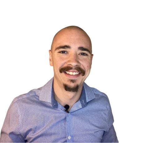 Ein Mann mit rasiertem Kopf, Schnurrbart und Spitzbart lächelt in die Kamera. Er trägt ein blau gemustertes Hemd und ein Ansteckmikrofon - bereit für den Spot des Influencer Award 2025 - vor einem weißen Hintergrund.