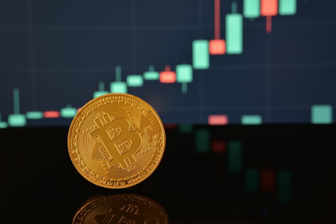 Eine physische Bitcoin-Münze steht vor einem unscharfen digitalen Candlestick-Diagramm, das die Kursentwicklung von Kryptowährungen zeigt und die Überschneidung von traditionellen Anlagen wie Almonty Industries und digitalen Vermögenswerten hervorhebt.