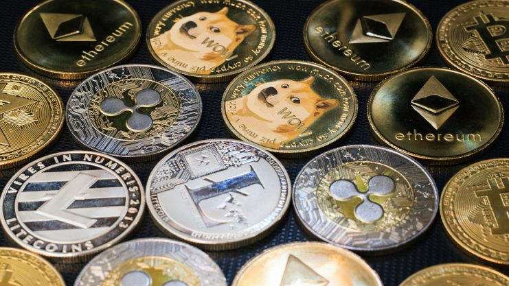 Eine Nahaufnahme verschiedener physischer Kryptowährungsmünzen, darunter Bitcoin, Ethereum, Litecoin, Ripple, Dogecoin und andere beliebte Altcoin-Token, die auf einer dunklen Oberfläche angeordnet sind.