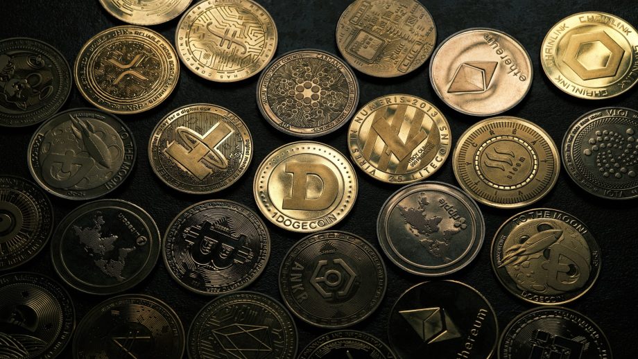 Verschiedene physische Münzen mit verschiedenen Kryptowährungslogos, darunter Bitcoin, Ethereum, Dogecoin und andere, sind in Reihen auf einer dunklen Oberfläche angeordnet und fangen den vielfältigen Geist von Altseason ein.