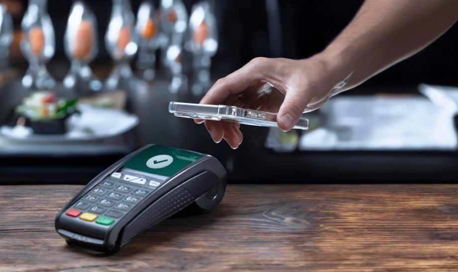 Eine Person hält ihr Smartphone über ein Zahlungsterminal, um in einem Restaurant kontaktlos mit Binance Pay zu bezahlen.