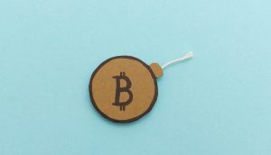 Ein runder, brauner Papierausschnitt mit einem fetten Bitcoin-Symbol und einer Schnur, die wie eine Bitcoin-Bombe aussieht, ist auf einem hellblauen Hintergrund platziert.