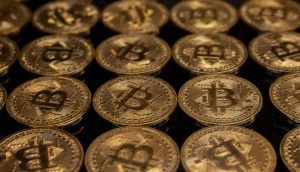 Reihen von goldfarbenen Münzen mit dem Bitcoin-Symbol sind auf einer dunklen Fläche dicht aneinandergereiht und unterstreichen die Anziehungskraft von Bitcoin.