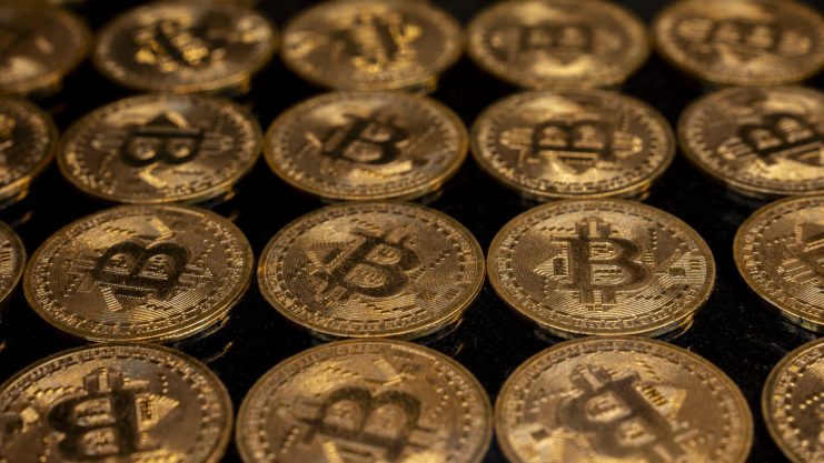 Reihen von goldfarbenen Münzen mit dem Bitcoin-Symbol sind auf einer dunklen Fläche dicht aneinandergereiht und unterstreichen die Anziehungskraft von Bitcoin.