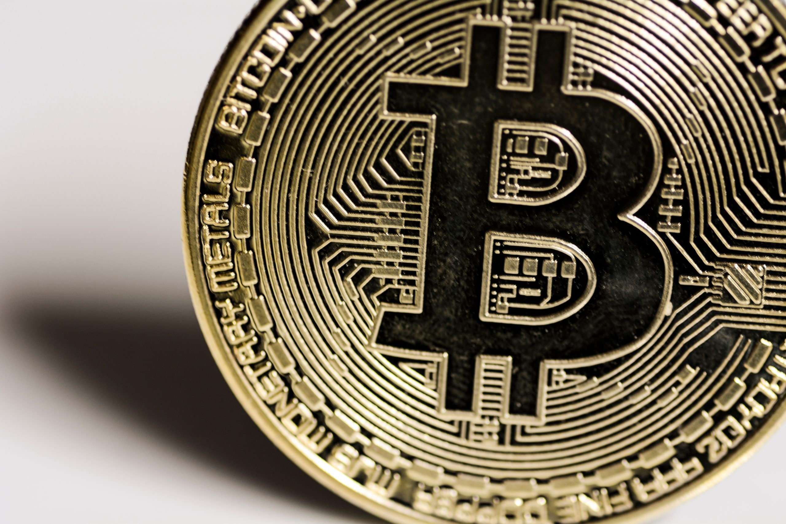Nahaufnahme einer physischen Bitcoin-Münze mit dem ikonischen Bitcoin-Symbol, kreislaufähnlichen Mustern und den Worten BITCOIN und MONETARY METALS am Rand.