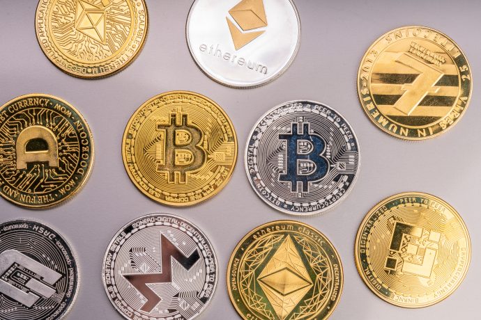Verschiedene physische Münzen, die verschiedene Kryptowährungen repräsentieren, darunter Bitcoin, Ethereum, Litecoin und Monero, ausgestellt auf einer hellen Oberfläche. Die herausragende Bitcoin-Münze sticht aus der Sammlung hervor.