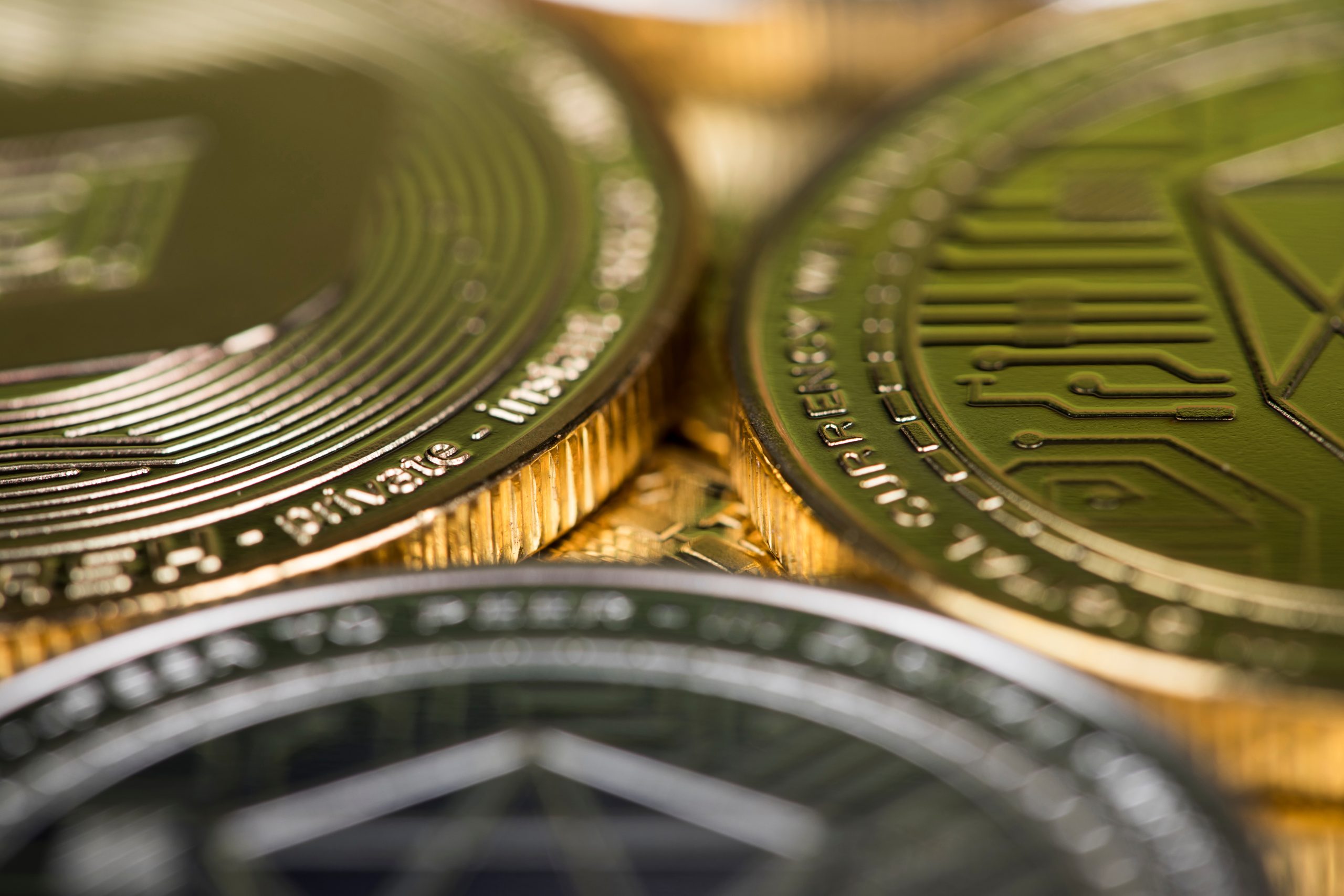 Nahaufnahme von drei Krypto-Münzen vor einem goldenen Hintergrund