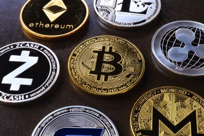 Eine Nahaufnahme verschiedener physischer Kryptowährungsmünzen, darunter Bitcoin, Ethereum und XRP, die auf einer dunklen Oberfläche angeordnet sind.