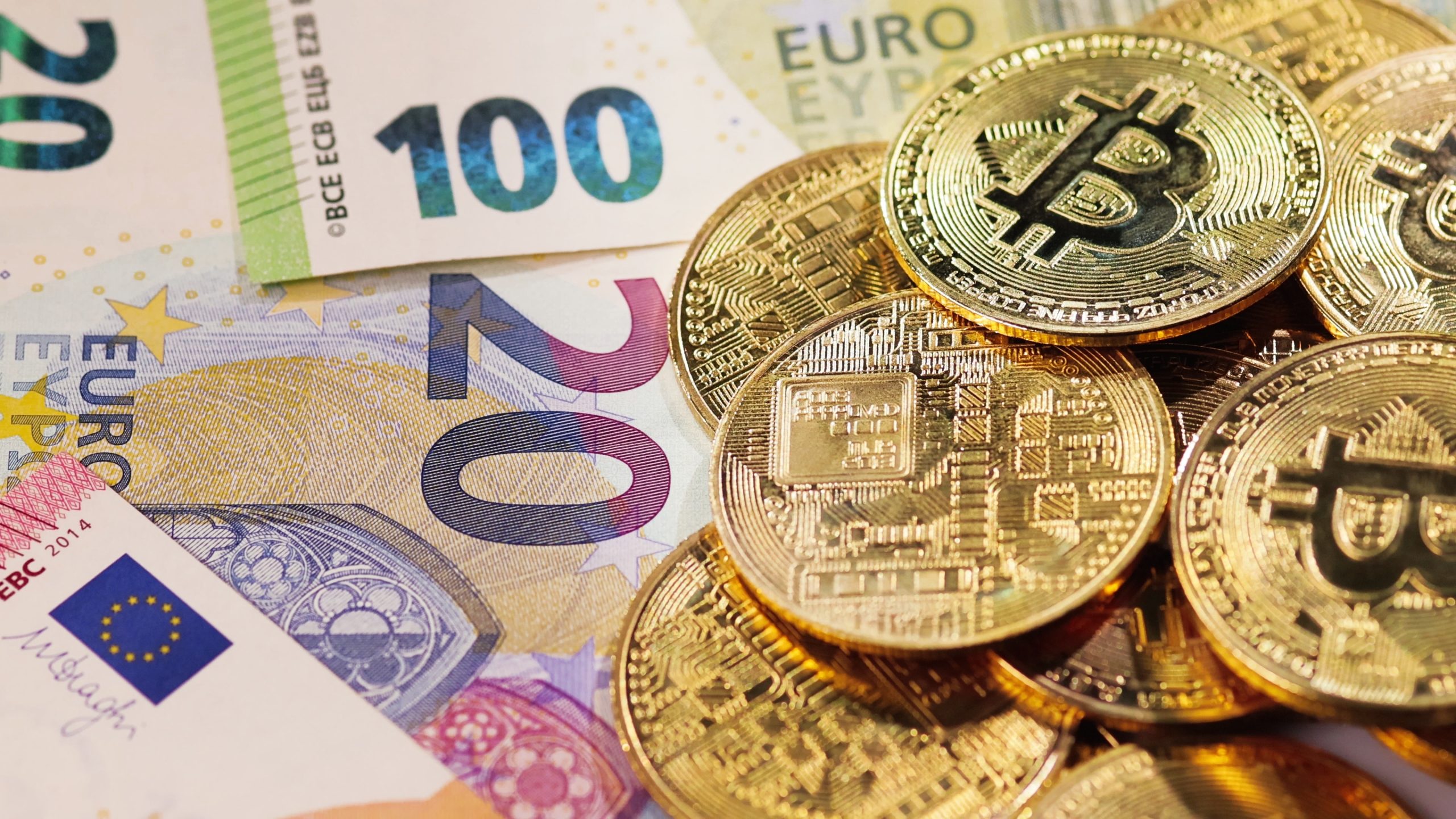 Euro-Banknoten liegen verstreut unter einem Haufen glänzender Bitcoin-Münzen und symbolisieren die dynamische Beziehung zwischen traditionellen Währungen und Kryptowährungen.
