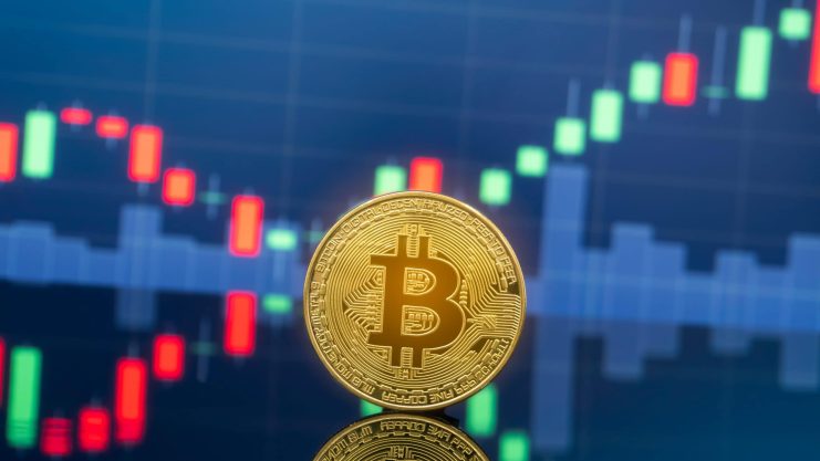 Eine goldene Bitcoin-Münze steht vor einem digitalen Bildschirm, der ein buntes Candlestick-Diagramm anzeigt, das die aktive Bitcoin-Handelsaktivität hervorhebt.