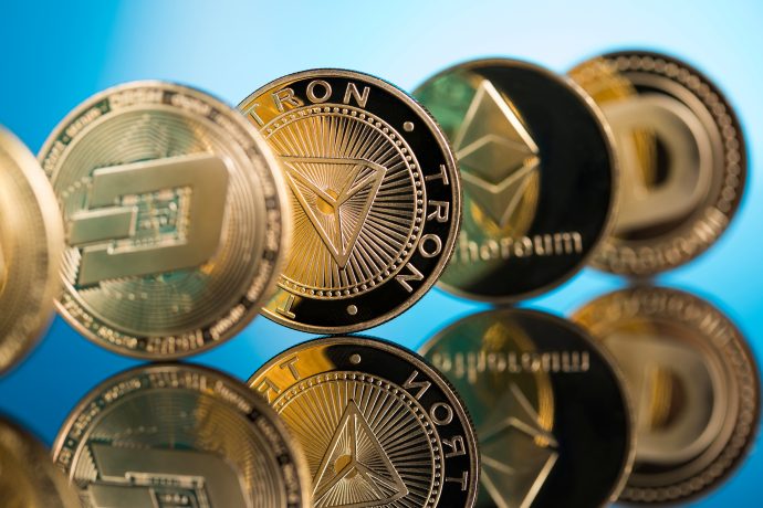 Eine Nahaufnahme von physischen Münzen, die verschiedene Kryptowährungen repräsentieren, darunter Bitcoin, Tron, Ethereum und Dash, aufrecht stehend und auf einer glänzenden Oberfläche reflektiert.