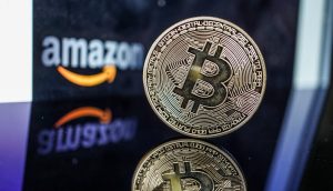 Eine physische Bitcoin-Münze steht aufrecht auf einer spiegelnden Oberfläche, mit dem verschwommenen Amazon-Logo im Hintergrund, um die wachsende Präsenz von Bitcoin im digitalen Handel hervorzuheben.